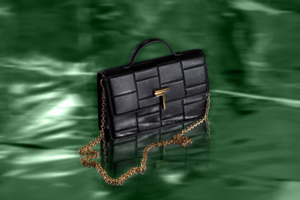 A black Trevony Minerva handbag with gold hardware and chain, set against a reflective green surface.